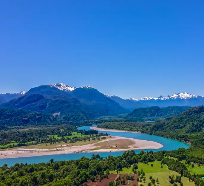 Vista aérea del río Risopatrón serpenteando entre un valle verde, rodeado de bosques nativos y montañas con cumbres nevadas bajo un cielo despejado.