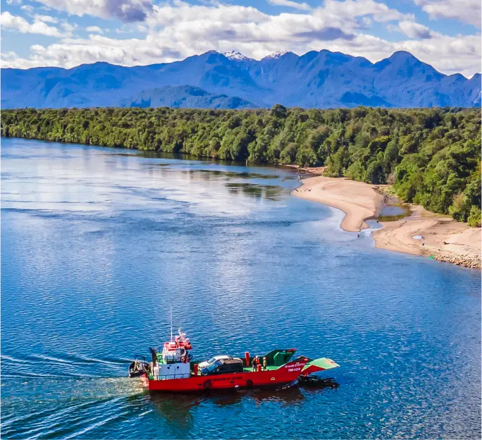 Embarcación navegando por el río Palena, con aguas amplias y tranquilas, bordeadas por bosques densos y una cordillera montañosa al fondo.